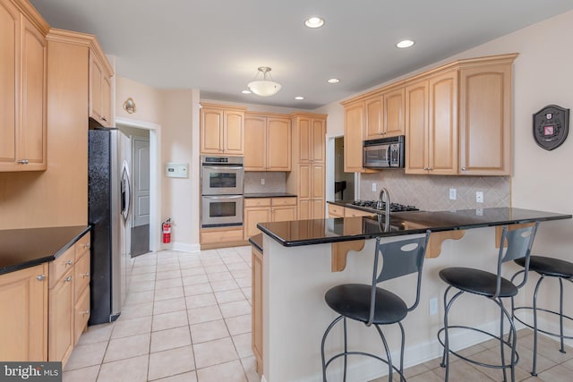 kitchen featuring a peninsula, a kitchen bar, stainless steel appliances, and light brown cabinetry