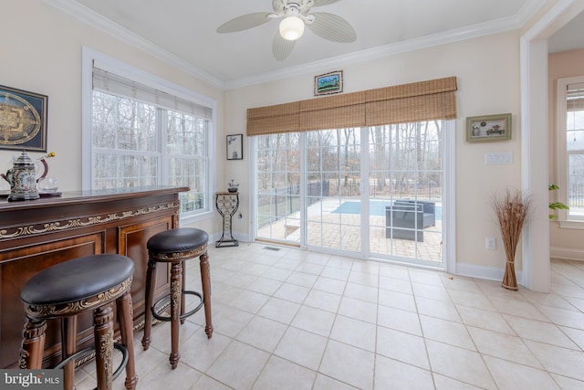 dining area featuring a dry bar, light tile patterned floors, ornamental molding, a ceiling fan, and baseboards