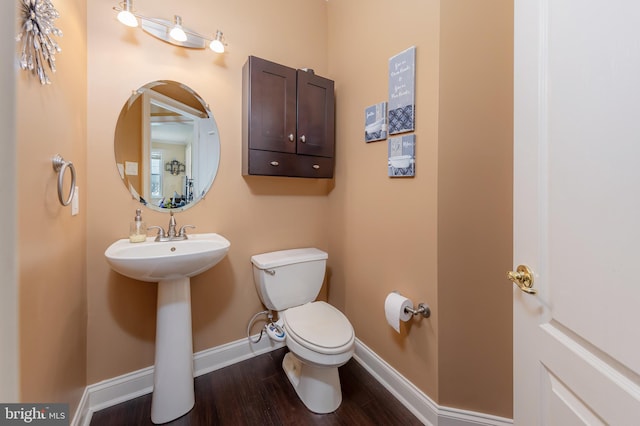 half bath featuring a sink, wood finished floors, toilet, and baseboards