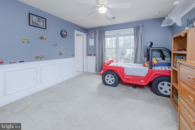 bedroom with a wainscoted wall, ceiling fan, carpet, and visible vents