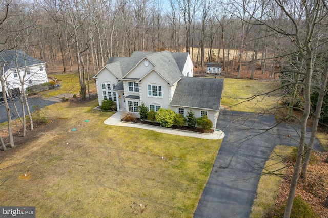 traditional-style house featuring driveway, stucco siding, a shingled roof, and a front yard