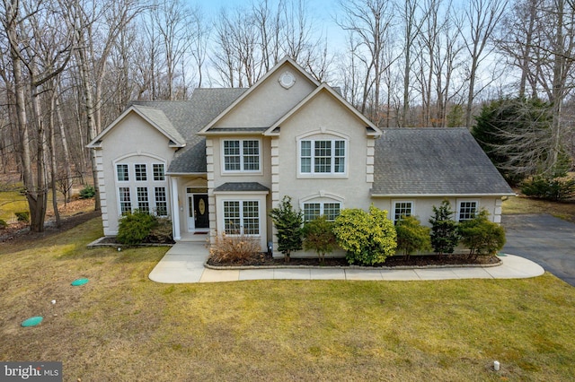 view of front of home featuring roof with shingles, a front yard, and stucco siding