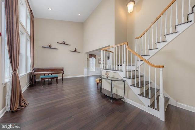 stairway with plenty of natural light, wood finished floors, a towering ceiling, and baseboards