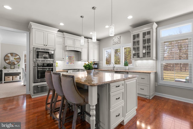 kitchen with a sink, a kitchen island, stainless steel appliances, a breakfast bar area, and glass insert cabinets