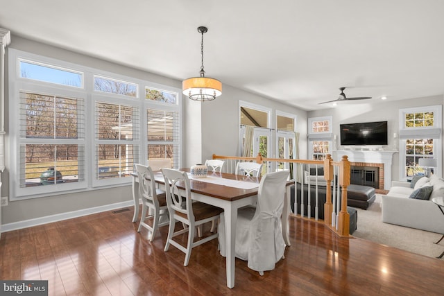 dining room with dark wood finished floors, a brick fireplace, a ceiling fan, and baseboards