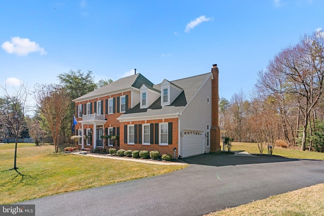 view of front facade with brick siding, a front yard, a chimney, a balcony, and driveway