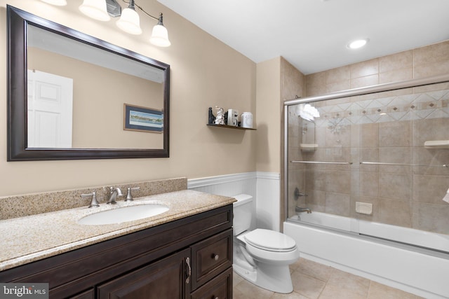 full bathroom with a wainscoted wall, toilet, combined bath / shower with glass door, tile patterned flooring, and vanity