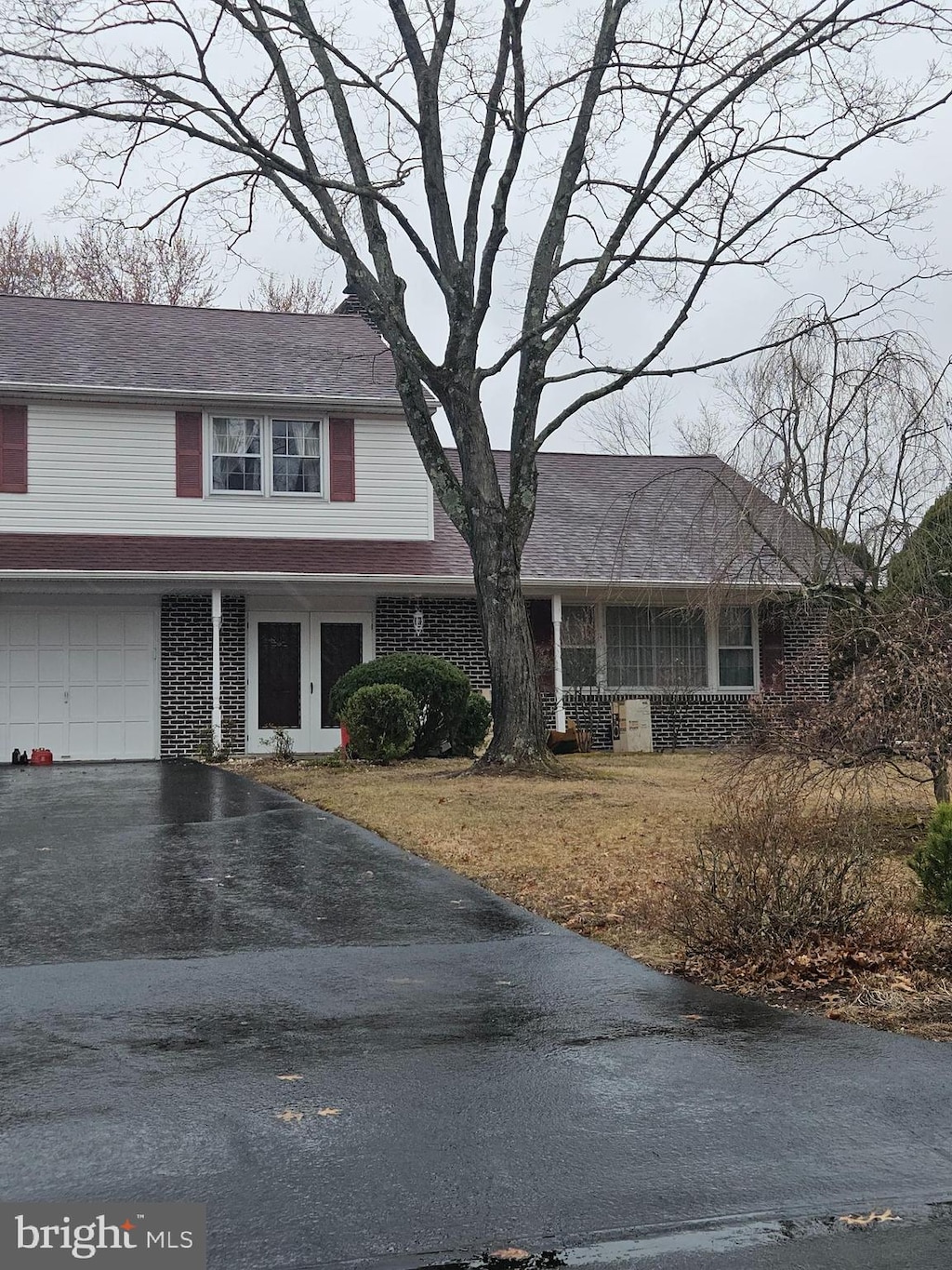 view of front of property featuring a porch, a garage, brick siding, driveway, and roof with shingles