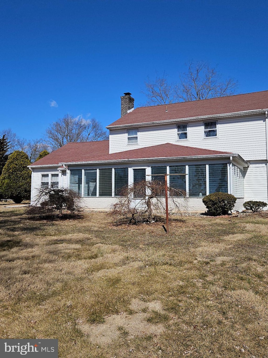 back of property featuring a sunroom, a chimney, and a yard