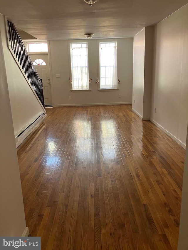 unfurnished living room featuring a baseboard heating unit, wood-type flooring, baseboards, and stairs