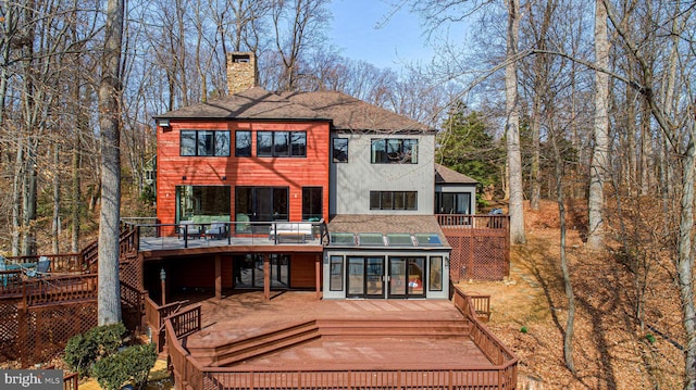 rear view of property with stucco siding, a chimney, a deck, and a shingled roof