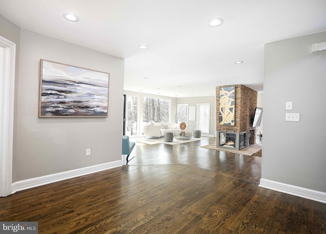 unfurnished living room featuring a multi sided fireplace, recessed lighting, baseboards, and wood finished floors