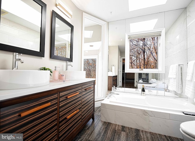 full bath featuring a bath, double vanity, wood finished floors, and a sink