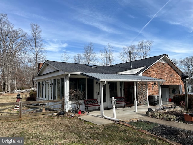 rear view of property with brick siding, a patio, a chimney, a sunroom, and metal roof