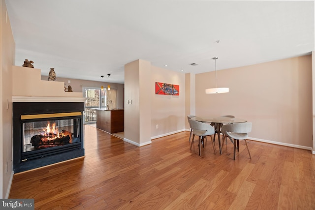 dining area with light wood-style floors, baseboards, visible vents, and a multi sided fireplace