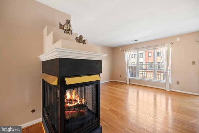 interior details featuring wood finished floors, a multi sided fireplace, visible vents, and baseboards