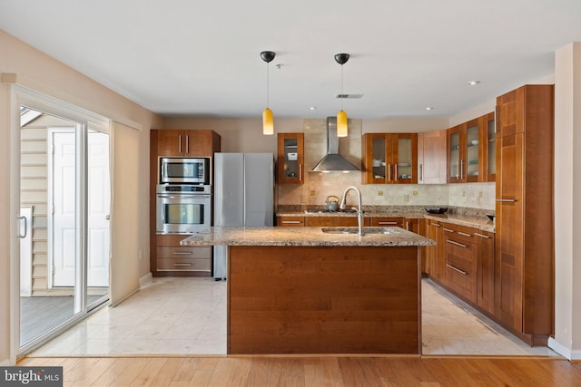 kitchen with decorative backsplash, wall chimney exhaust hood, brown cabinets, stainless steel appliances, and a sink