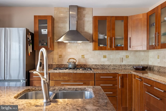 kitchen featuring light stone countertops, wall chimney exhaust hood, stainless steel appliances, and decorative backsplash