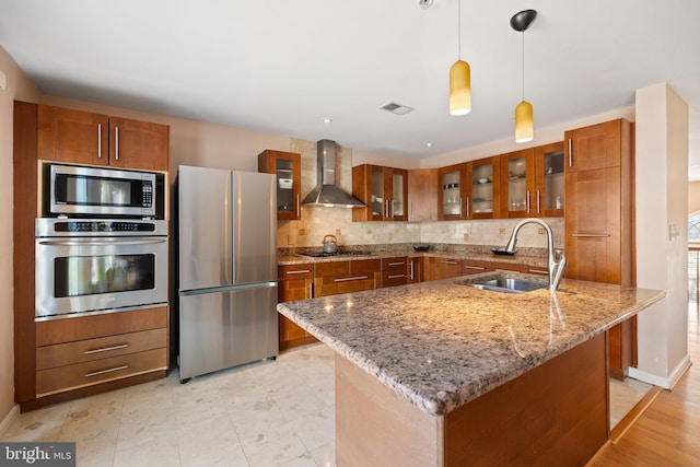 kitchen featuring stainless steel appliances, brown cabinetry, a sink, and wall chimney range hood