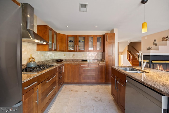 kitchen with visible vents, wall chimney exhaust hood, light stone counters, stainless steel appliances, and a sink