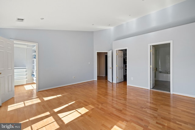 spare room featuring light wood-type flooring, visible vents, vaulted ceiling, and baseboards