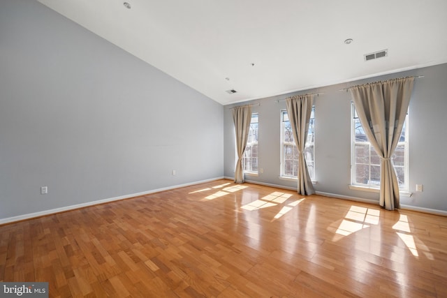 empty room featuring light wood-type flooring, visible vents, vaulted ceiling, and baseboards