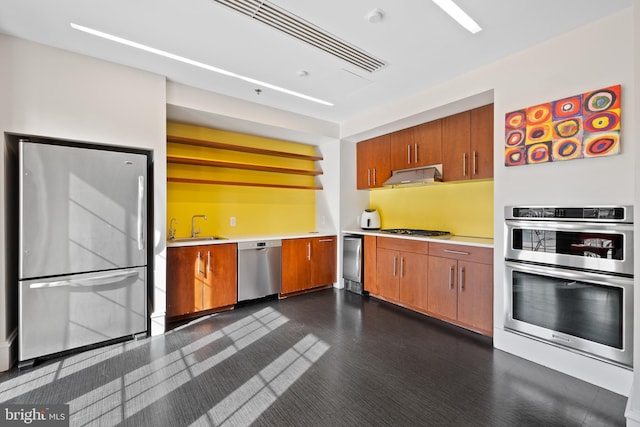 kitchen with brown cabinetry, stainless steel appliances, light countertops, under cabinet range hood, and a sink