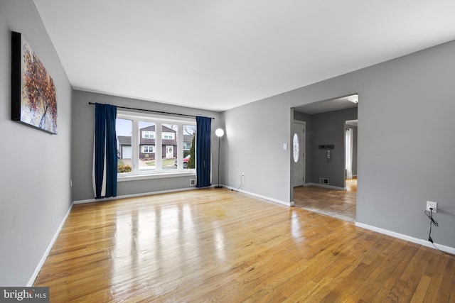 spare room featuring light wood finished floors, visible vents, and baseboards