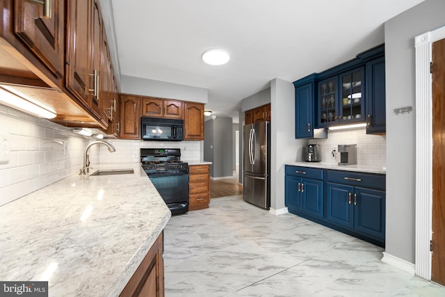 kitchen featuring a sink, marble finish floor, blue cabinetry, black appliances, and glass insert cabinets