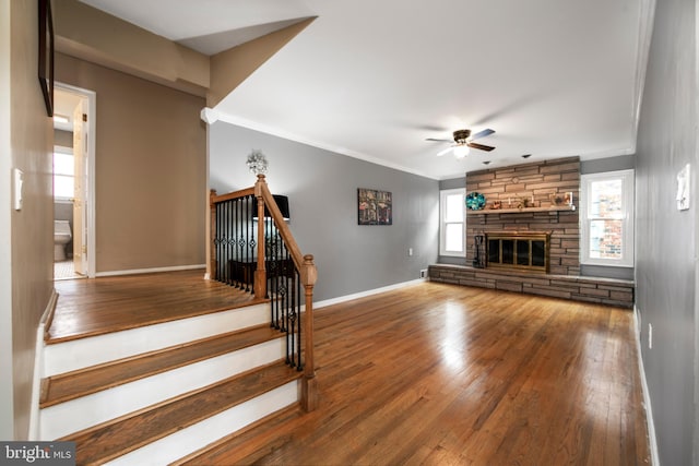 unfurnished living room featuring baseboards, a ceiling fan, hardwood / wood-style flooring, crown molding, and a fireplace