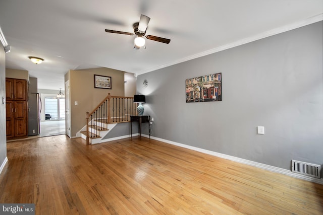 spare room featuring ceiling fan with notable chandelier, visible vents, baseboards, stairs, and light wood finished floors