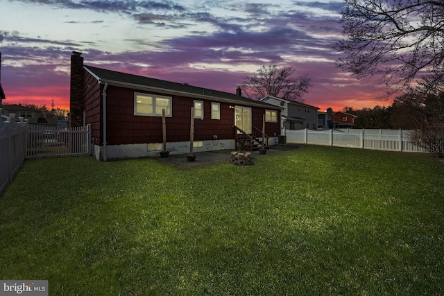 view of side of property with entry steps, a fenced backyard, a chimney, and a lawn