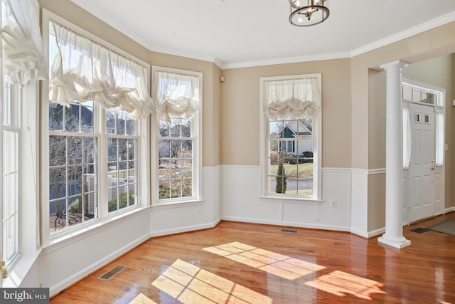 unfurnished dining area featuring crown molding, wood finished floors, visible vents, and ornate columns