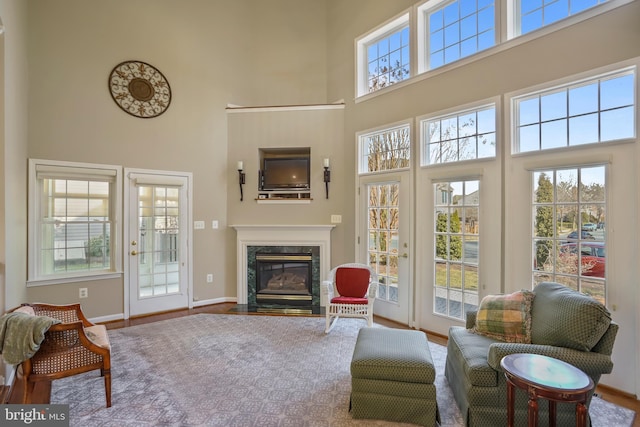 living room featuring a towering ceiling, a premium fireplace, baseboards, and wood finished floors