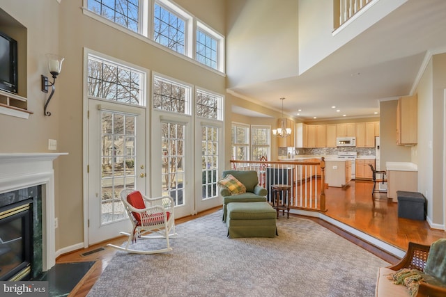 living room featuring baseboards, ornamental molding, wood finished floors, a chandelier, and a high end fireplace