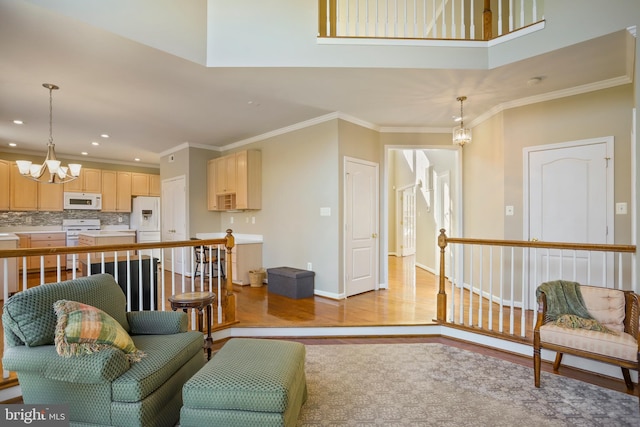 living area with baseboards, ornamental molding, light wood-style flooring, and a notable chandelier