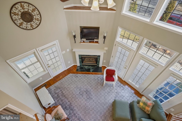 living area featuring a high ceiling, a fireplace, wood finished floors, visible vents, and baseboards