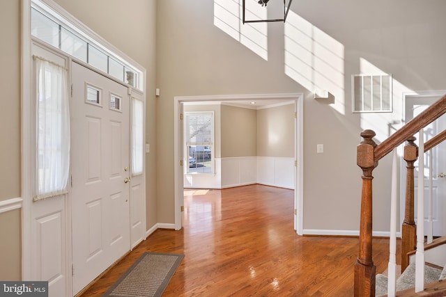 entryway featuring a towering ceiling, stairs, visible vents, and wood finished floors