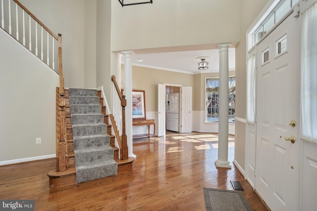 foyer entrance featuring ornamental molding, a high ceiling, wood finished floors, and ornate columns