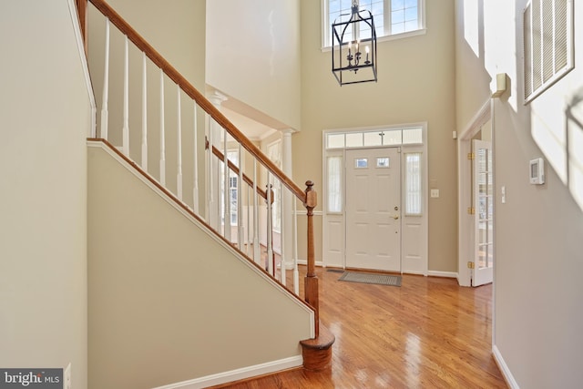 foyer entrance with baseboards, a towering ceiling, wood finished floors, stairs, and a chandelier