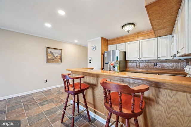 kitchen with a breakfast bar area, white cabinets, baseboards, and freestanding refrigerator