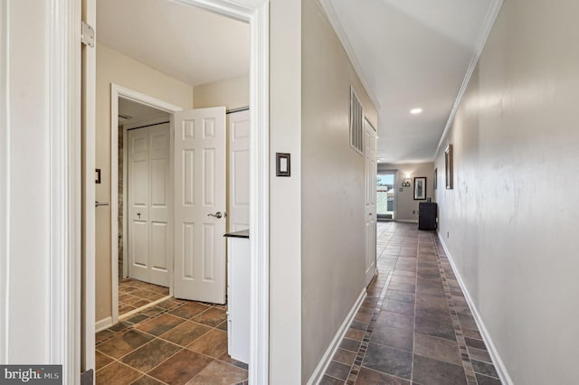 corridor featuring stone finish floor, crown molding, and baseboards