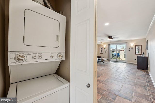 clothes washing area featuring stacked washer and clothes dryer, crown molding, baseboards, ceiling fan, and laundry area