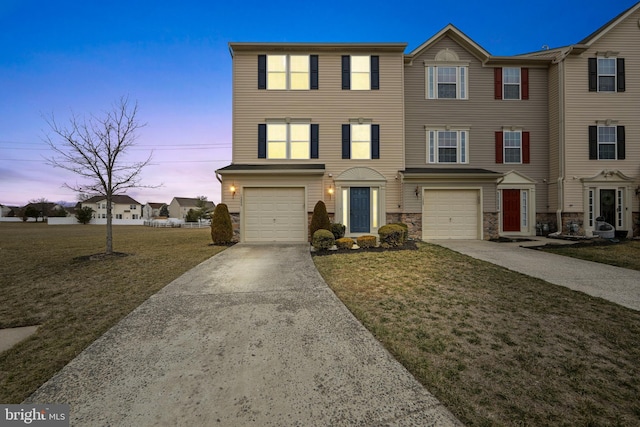 townhome / multi-family property with stone siding, driveway, an attached garage, and a front yard