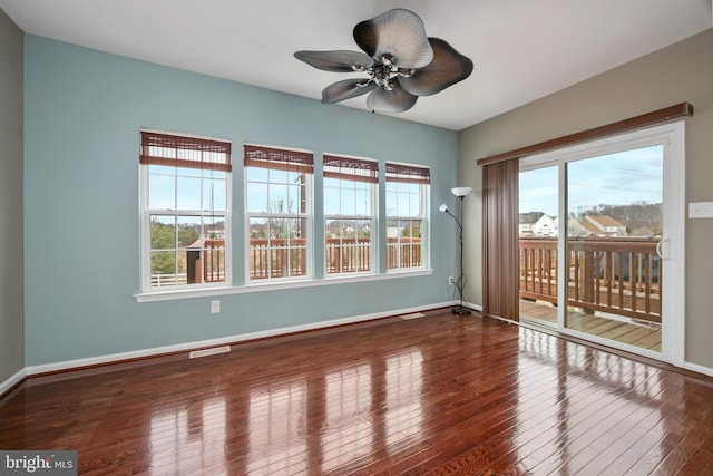 empty room with hardwood / wood-style flooring, a ceiling fan, baseboards, and visible vents