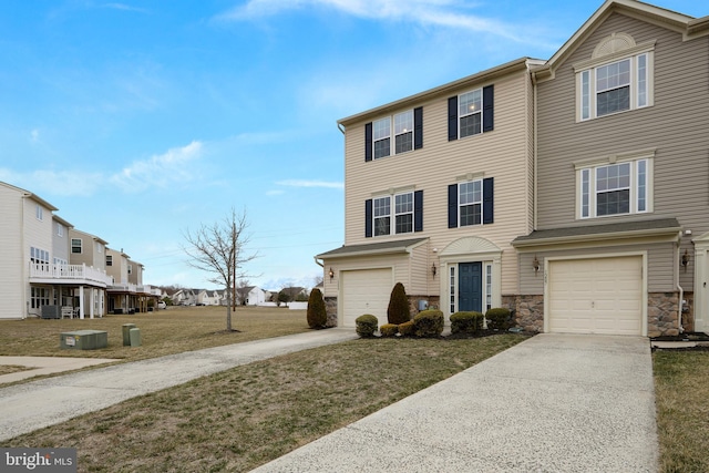 townhome / multi-family property featuring stone siding, a residential view, concrete driveway, a front yard, and an attached garage