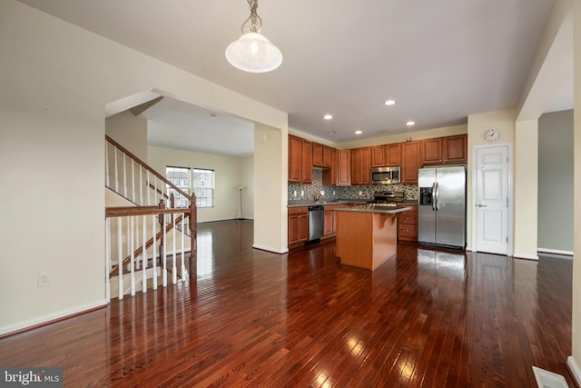 kitchen featuring dark wood-style flooring, stainless steel appliances, decorative light fixtures, backsplash, and a center island