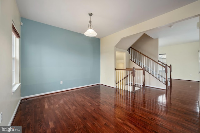 empty room with baseboards, wood finished floors, and stairs