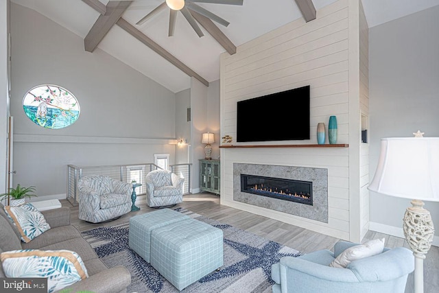 living room featuring baseboards, a glass covered fireplace, wood finished floors, high vaulted ceiling, and beam ceiling