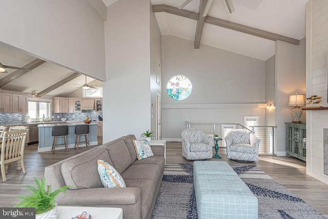 living area featuring a fireplace, a ceiling fan, wood finished floors, beamed ceiling, and baseboards